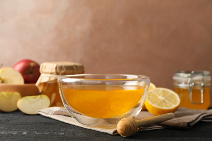 Bowl with honey, dipper and fruits on wooden background, space for text