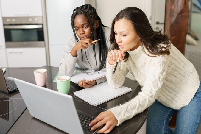 Two women sitting at kitchen table concentrating on their work on a pc