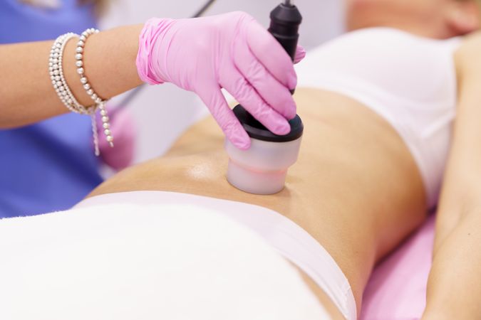 Professional in scrubs performing cosmetic procedure on stomach