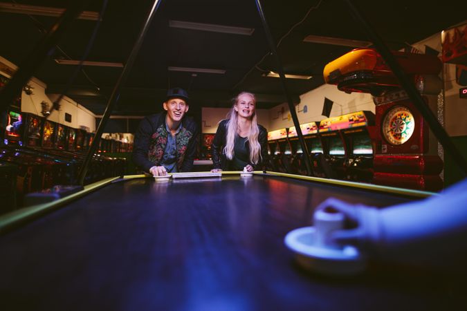 Man and woman playing a game of air hockey in the game room at amusement park