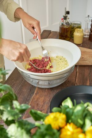 Crop woman mixing chopped meat with ingredients in bowl