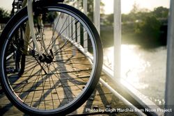 Wheel of bike on bridge looking down at sun on water 5RaWR0