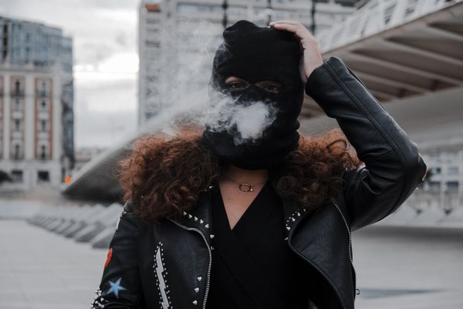 Woman in mask and jacket smoking on street