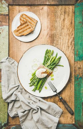 Asparagus and soft boiled egg on plate, with toast on wooden table with green trim