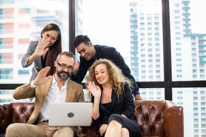 Group of colleagues in video call around leather sofa