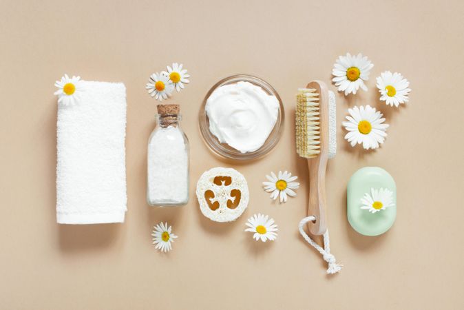 Relaxing bath salts and oils, loofah and brushes on beige with daisies