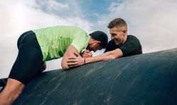 Men in an obstacle course climbing a drum