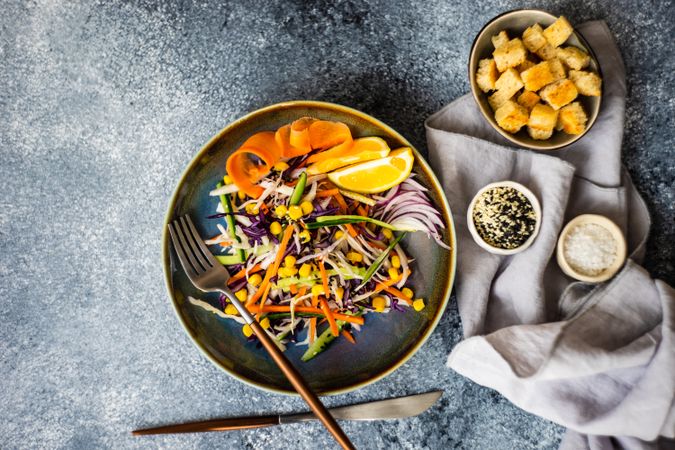 Top view of healthy vegetable salad and lemon slices in bowl on counter with copy space