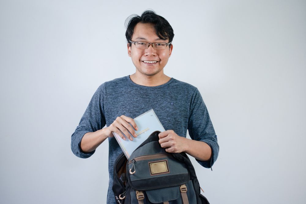 Asian student male looking for book in bag with happy gesture
