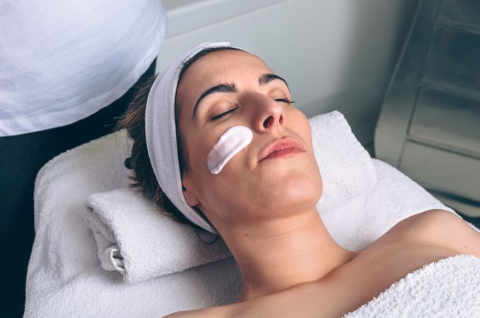 Woman lying with eyes closed having a clay mask applied