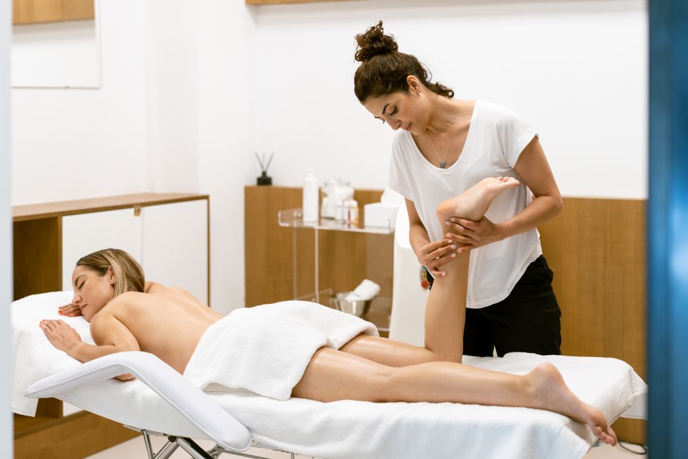 Skilled masseuse working on a female client’s legs