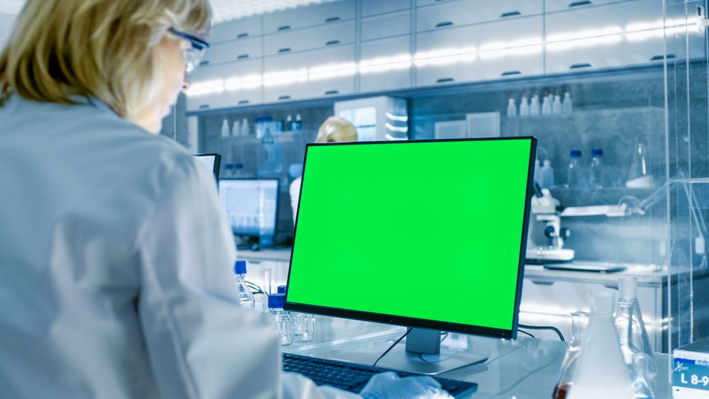 Female Scientist Working on her Computers (Mock-up Green Screen) In Modern Laboratory.