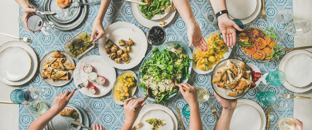 Group of people at blue patterned table with fresh fruits, salad, and vegetables, wide composition