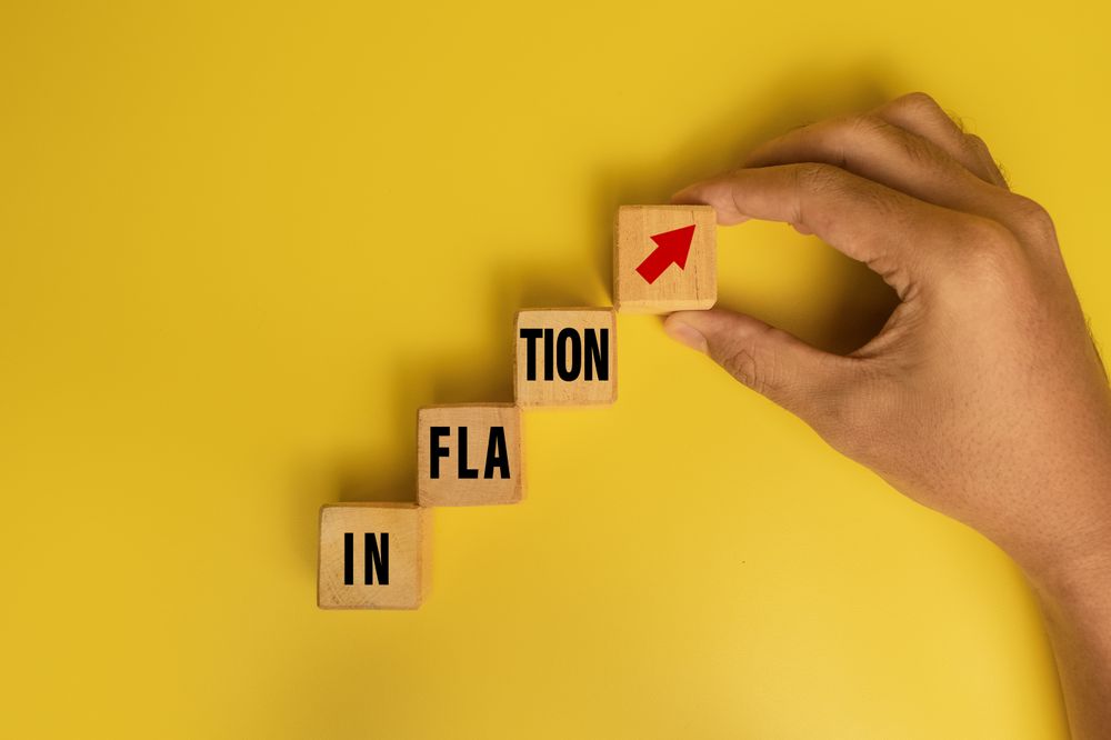 male hand put a wooden block with inflation word and red up arrow isolated on yellow background. concept of rising inflation rate