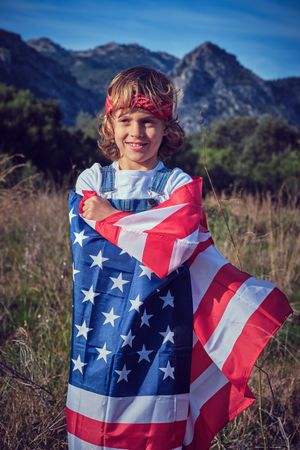 Cheerful preteen boy wrapping in American national flag