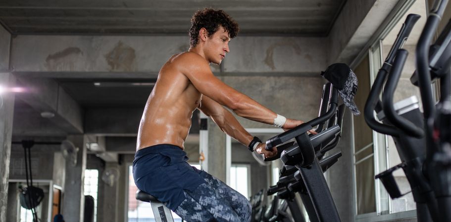 Side view of muscular white man working out on cycling machine