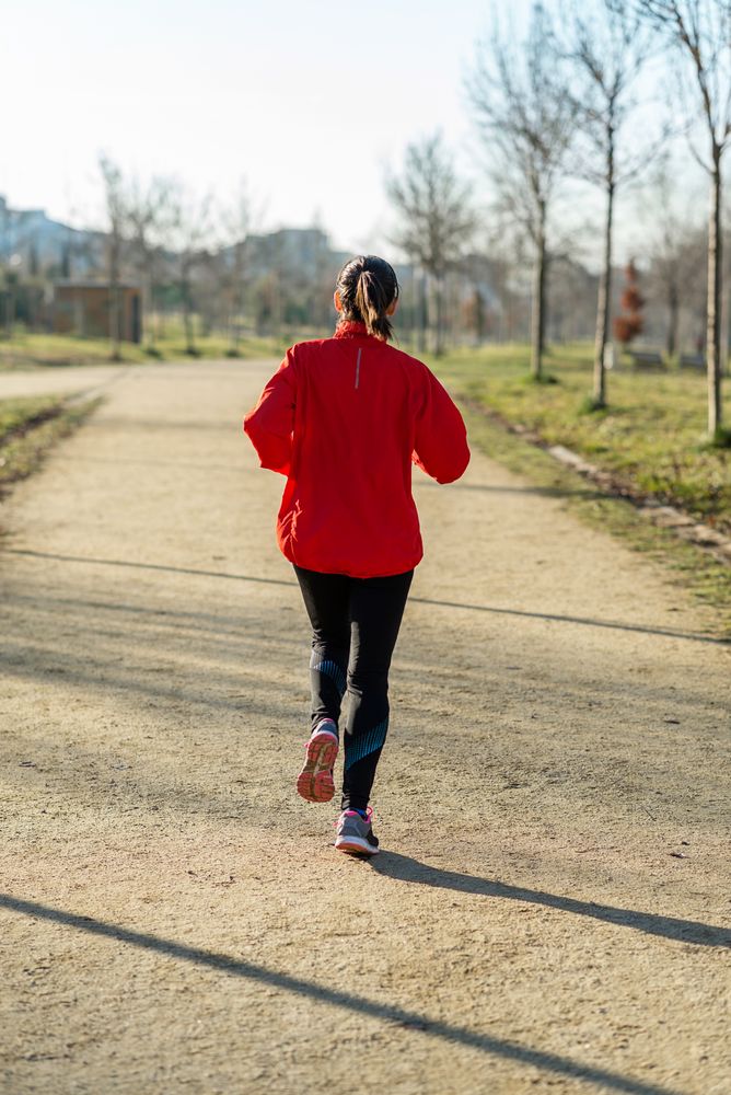 Back of fit woman jogging outdoors in park on sunny autumn day
