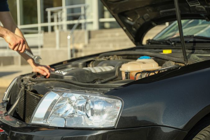 A man holds a wrench over a car engine. Car inspection