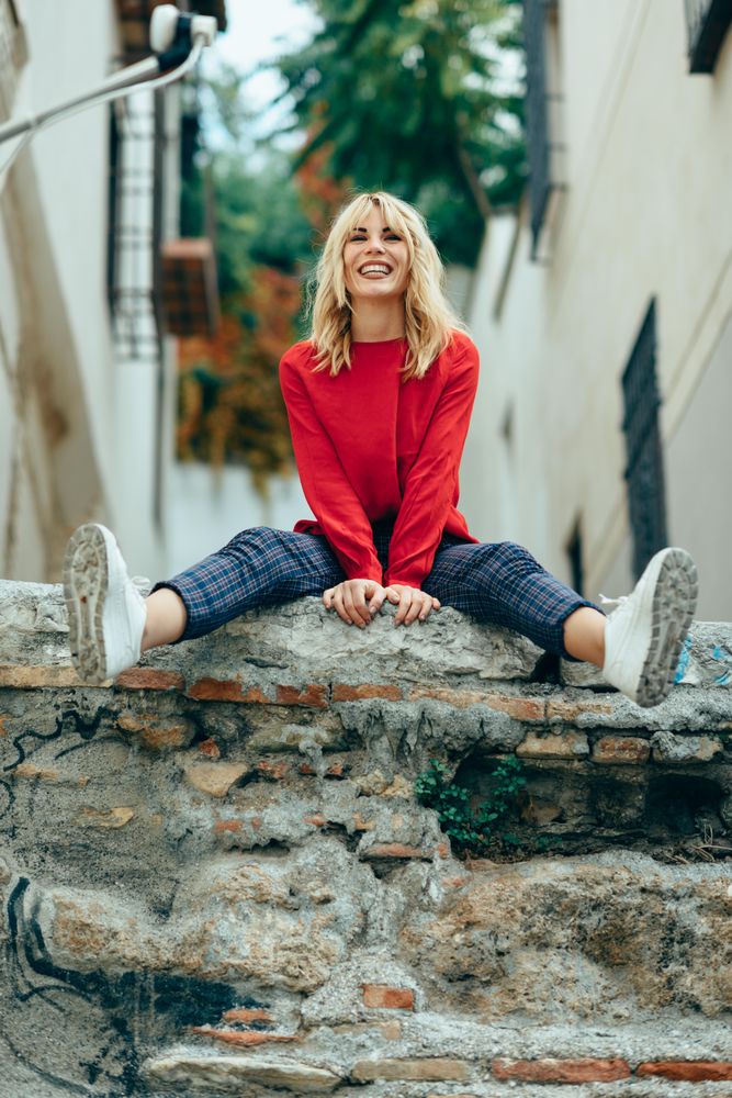 Smiling blond woman sitting on stone wall with her legs extended