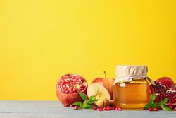 Apples, pomegranate, and honey pot in bright yellow room with copy space