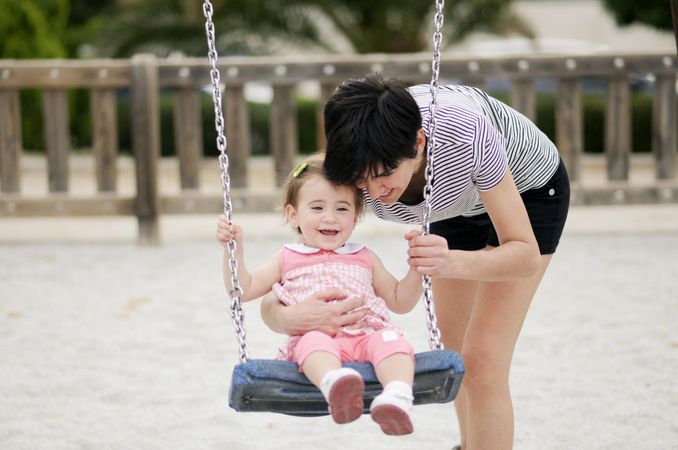 Woman with girl on swing in park