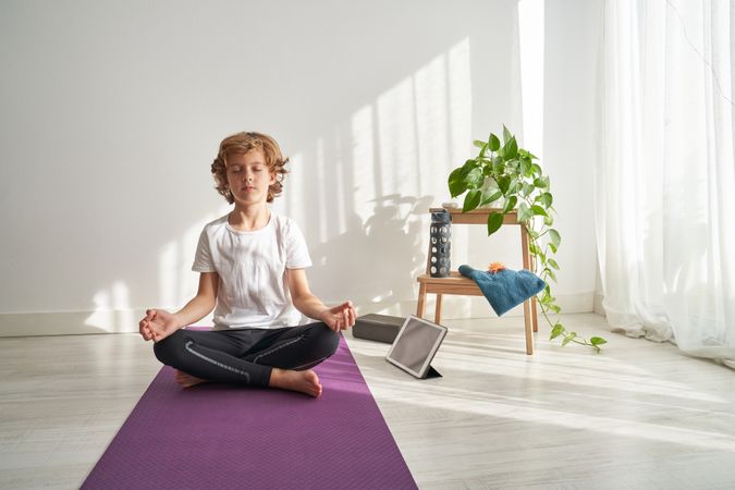 Focused preteen boy sitting in Lotus pose on yoga mat