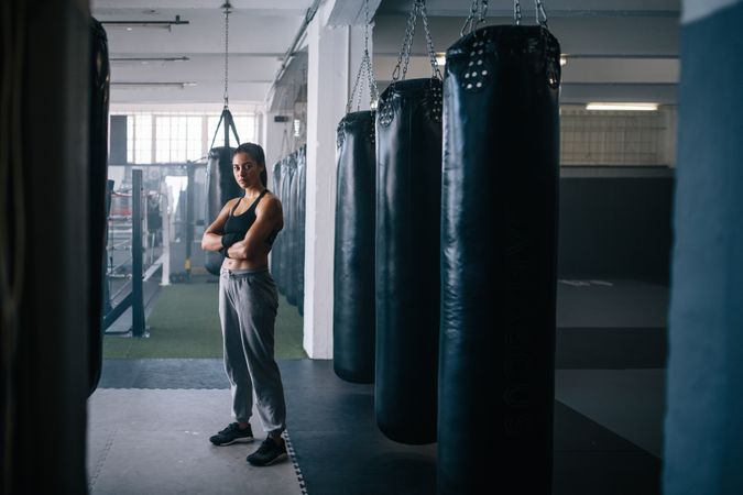 Portrait of female boxer standing among punching bags in studio