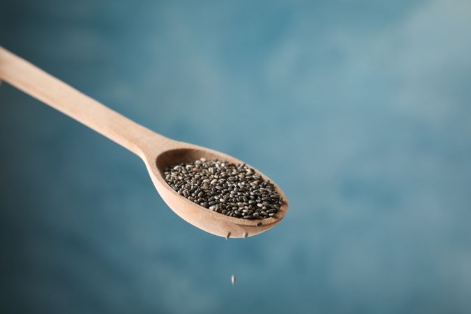 Chia seeds and spoon against blue background, close up