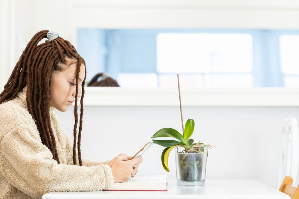 Woman with braids browsing a phone while sitting at a table