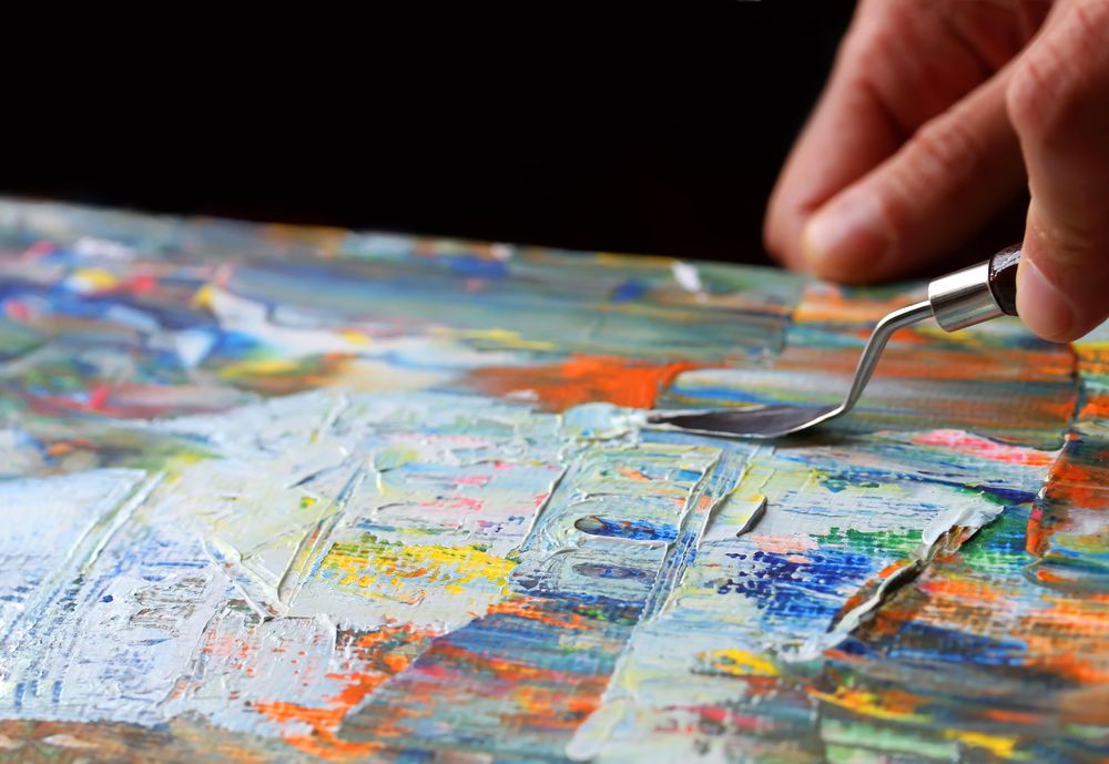 A hang holding a palette knife to a canvas