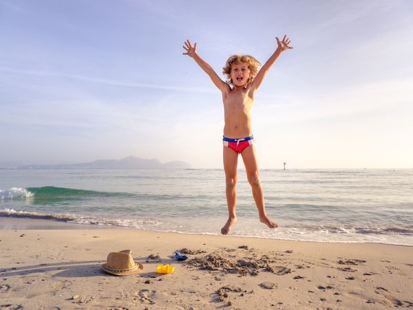 Happy boy raising arms and jumping on sandy beach