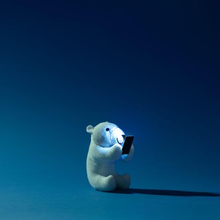 Polar bear toy with mobile phone on night blue background