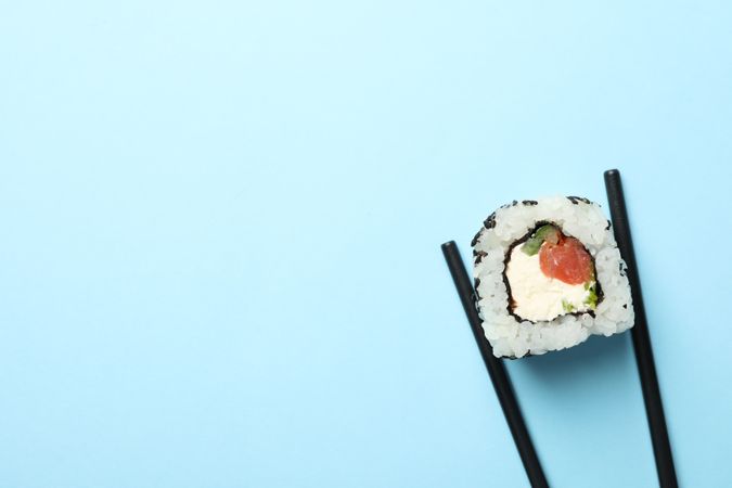 Chopsticks with sushi roll on blue background, space for text. Japanese food