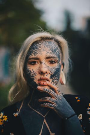 Edgy young blonde woman with cross-hatch facial tattoos and multiple piercings