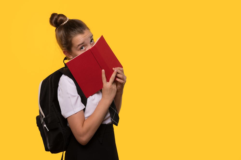 Schoolgirl hides face behind book.