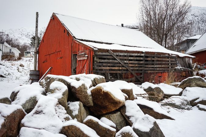 Large red barn against snowy hill and residential houses in countryside