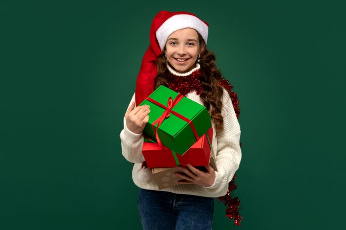 Smiling girl in Santa hat holding Christmas presents.