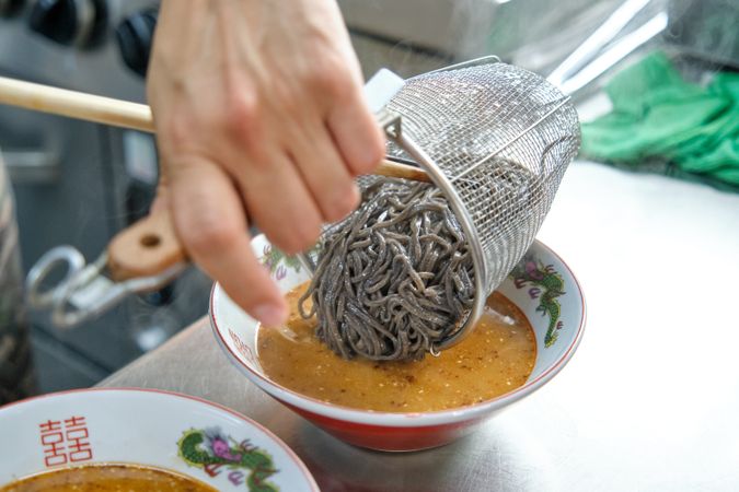 Cook adding boiled noodles to bowl of broth