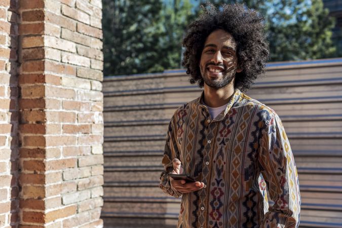 Smiling man using a mobile phone while standing outdoors on a sunny day