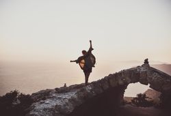 Woman with arms outstretched on castle wall overlooking sea