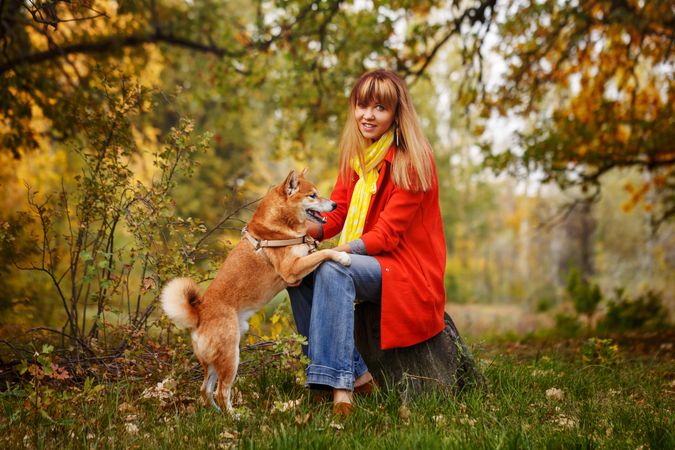 Female in red coat sitting with dog in park surrounded by fall leaves