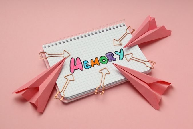 Notepad with “memory” written in colorful markers with arrow shaped paper planes and paper clips