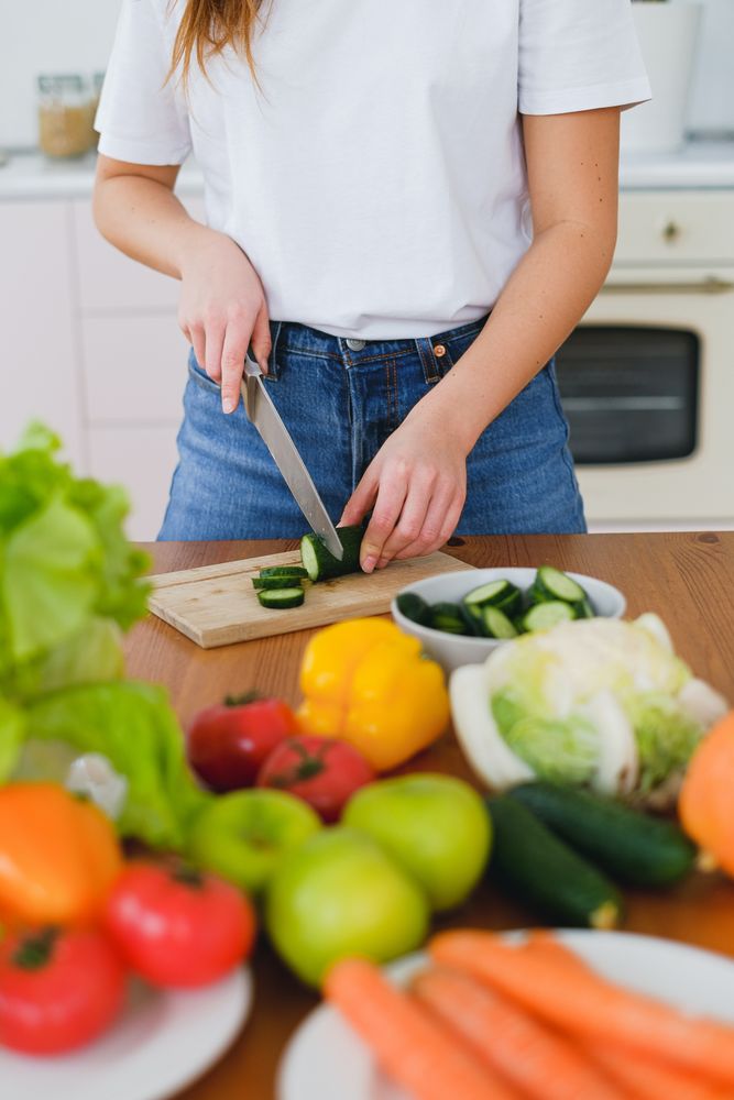 Cropped image of woman slicing a cucumber on brown wooden chopping board