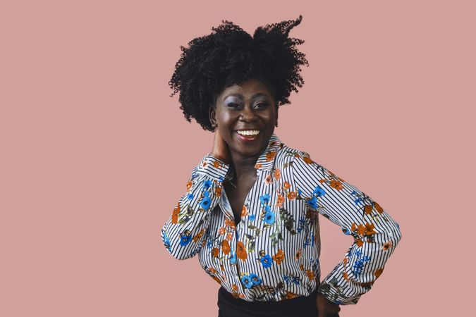 Studio shot of Black woman in floral print shirt with one hand at her ear and one on her hip