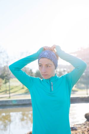 Woman in ear warmers adjusting hair while working out outdoors on sunny fall day