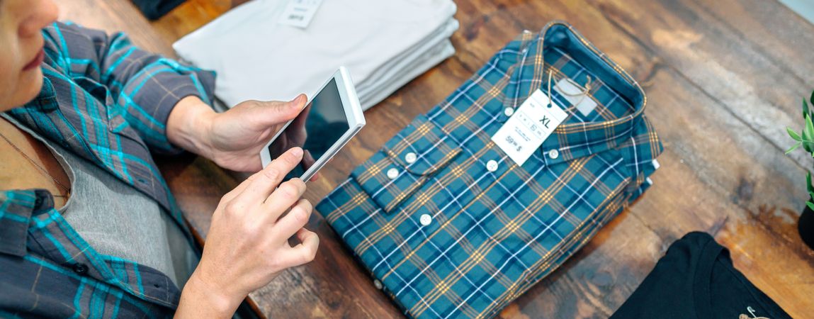 Banner of young female customer taking photo of plaid shirt over counter in clothes shop