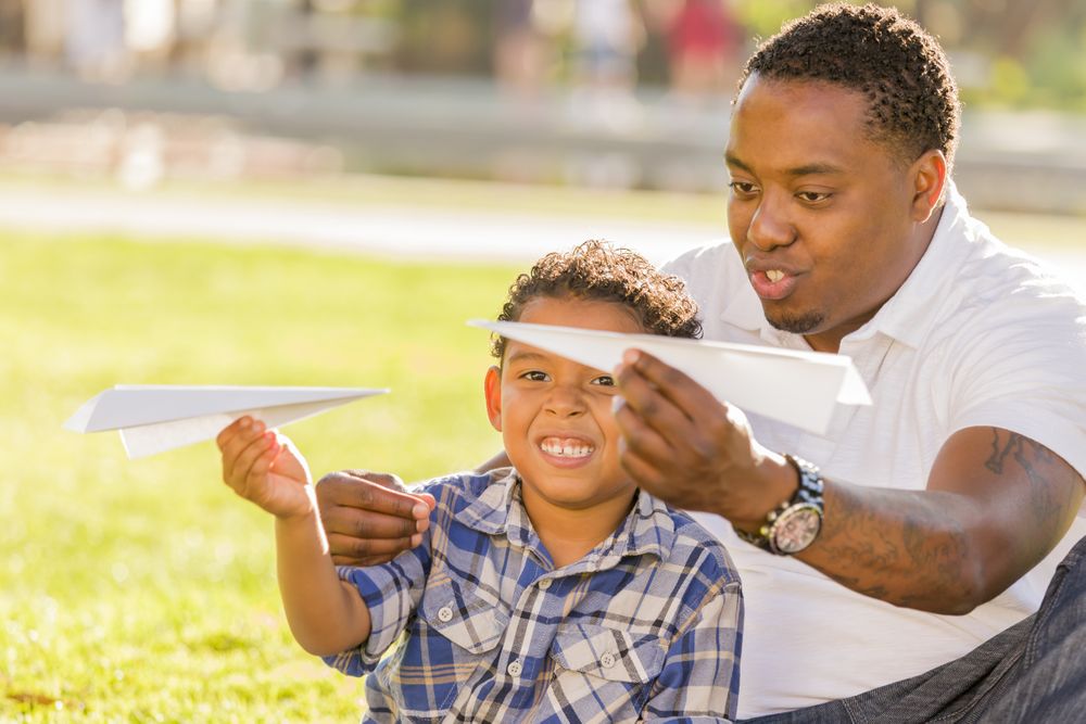 Father and Son Playing with Paper Airplanes in sunny park