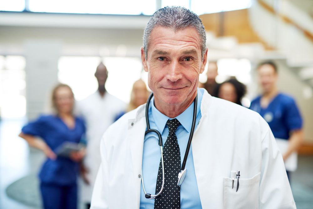 Portrait of mature doctor in lab coat and stethoscope with his team in the background