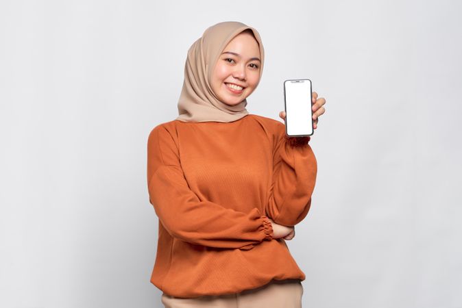 Confident Muslim woman smiling while holding up smart phone mock up