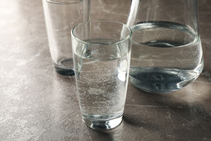 Glasses of water and pitcher on grey marble table